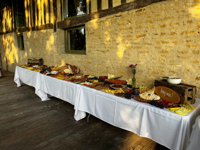 Grand buffet grazing table de mariage garni de charcuteries, fromages et fruits frais le long d'un mur en pierres apparentes pour vin d'honneur organisé par votre wedding planner de Seine et Marne