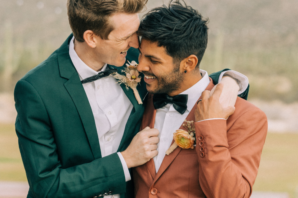 Deux jeunes mariés souriants et complices en costumes vert et terracotta lors de leur séance photo de mariage